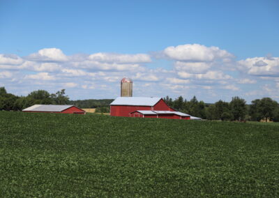 Landscape photo of a field, red barn, silo and sky with clouds